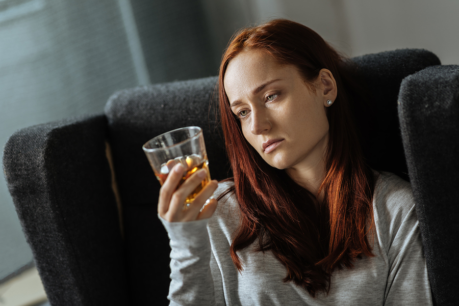 A woman alone in her house looking at a glass of whiskey.