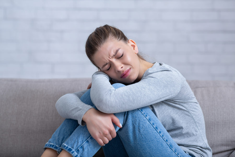 A woman suffering from trauma, hugging her knees on the couch.